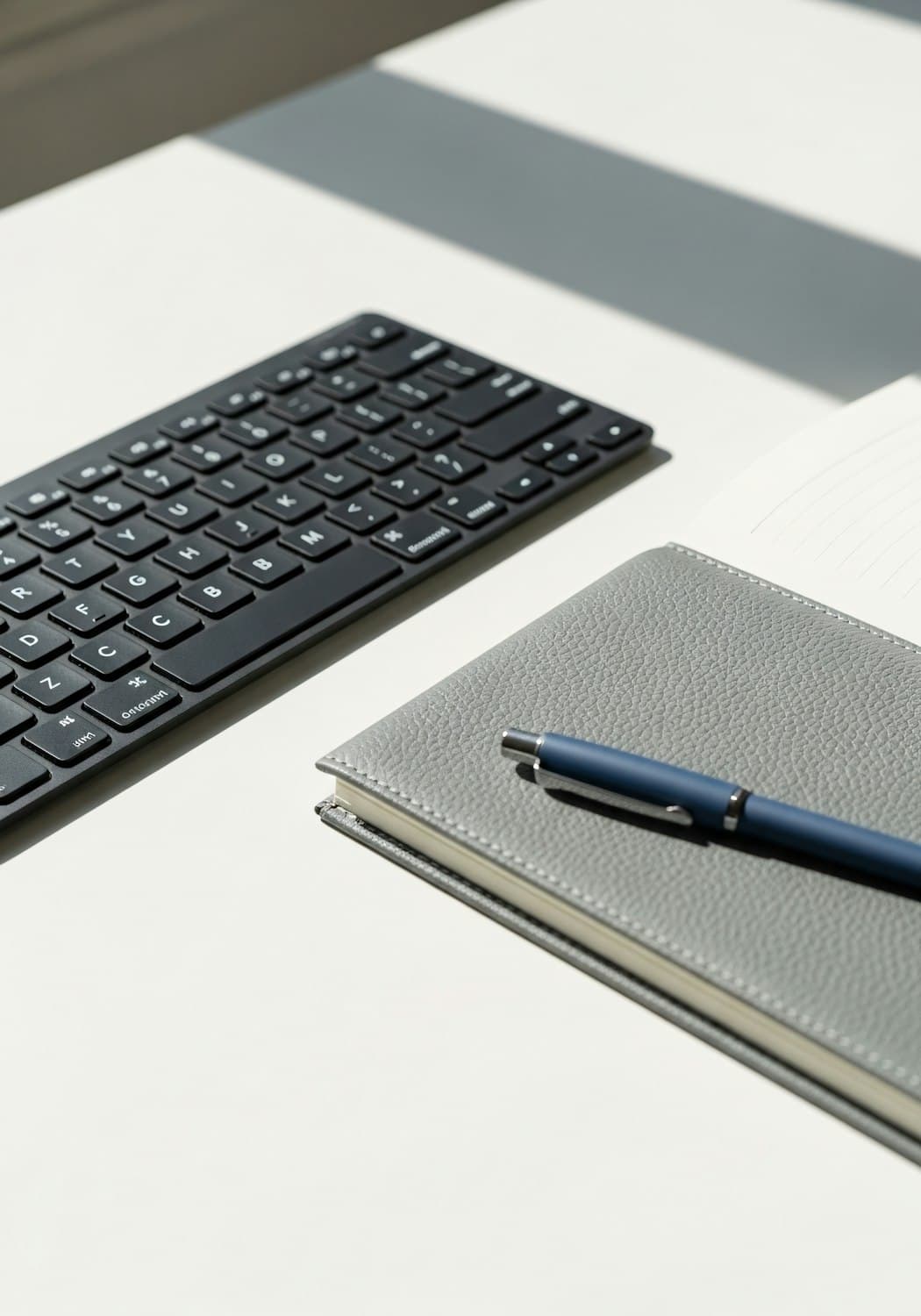 Clavier, carnet en cuir et stylo posés sur un bureau clair